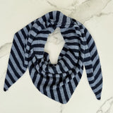 A triangular knit scarf with horizontal navy and light gray stripes, styled in a loop on a white marble surface.