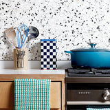 Kitchen scene with a blue pot on a stove, checkered towel, and green checkered towel hanging on an oven.