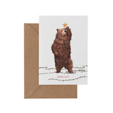 Greeting card with a bear wrapped in lights and a star on its head, with a brown envelope.