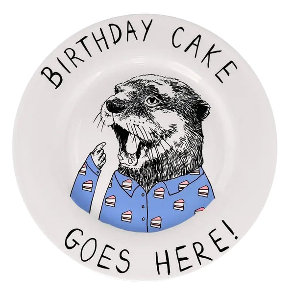 A white ceramic plate featuring a humorous illustration of an otter wearing a blue shirt with birthday cake slice patterns, surrounded by the text 'BIRTHDAY CAKE GOES HERE!'.