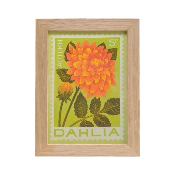 A framed botanical art print featuring an orange and yellow dahlia flower with green leaves on a light green background, enclosed in a light natural wood frame.