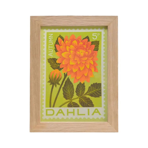 A framed botanical art print featuring an orange and yellow dahlia flower with green leaves on a light green background, enclosed in a light natural wood frame.