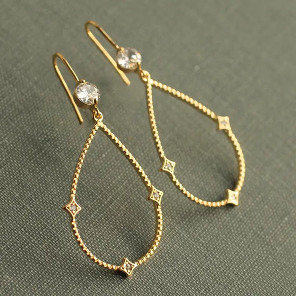 Gold teardrop earrings with small diamonds on a green fabric background
