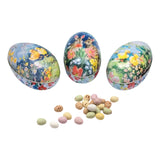 Three colorful Easter egg-shaped tins with floral and animal designs, containing small pastel candies.