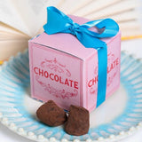 pink and red box tied up with blue ribbon with two chocolate truffles to the front