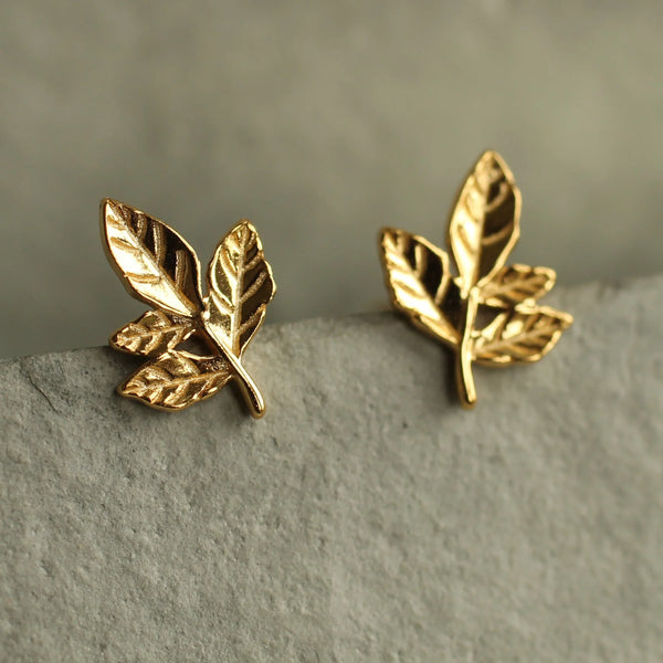 Gold leaf-shaped earrings on a textured surface with a neutral background
