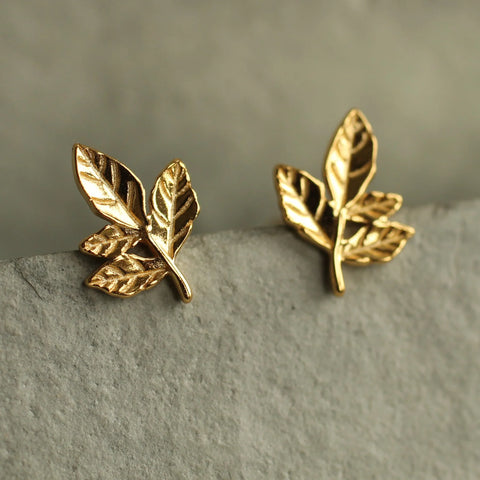 Gold leaf-shaped earrings on a textured surface with a neutral background