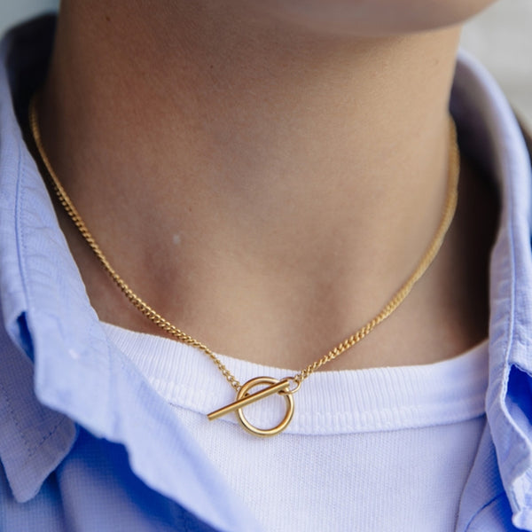 Gold necklace with a toggle clasp worn by a person against a white shirt background