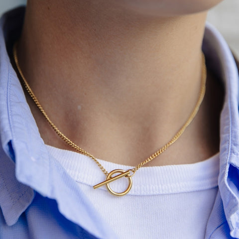 Gold necklace with a toggle clasp worn by a person against a white shirt background