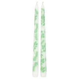 Two white taper candles with a light green herb leaf pattern, standing upright against a plain white background.