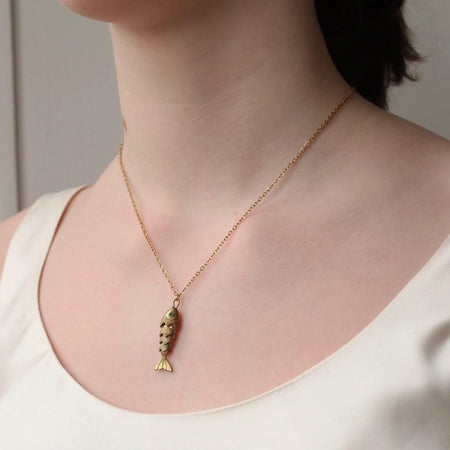 Gold moving fish necklace with a fish pendant worn by a person in a white top.
