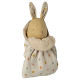 A  bunny with patterned ears, wrapped in a cream fabric swaddle blanket with pastel polka dots, on a solid white background