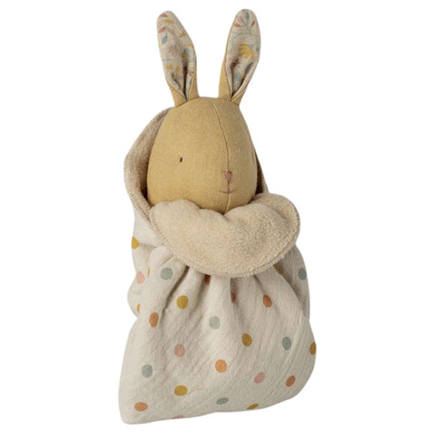 A  bunny with patterned ears, wrapped in a cream fabric swaddle blanket with pastel polka dots, on a solid white background