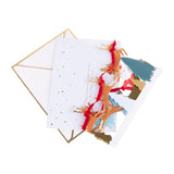 Greeting card with Christmas design featuring reindeer and christmas trees, accompanied by a gold envelope on a white background.
