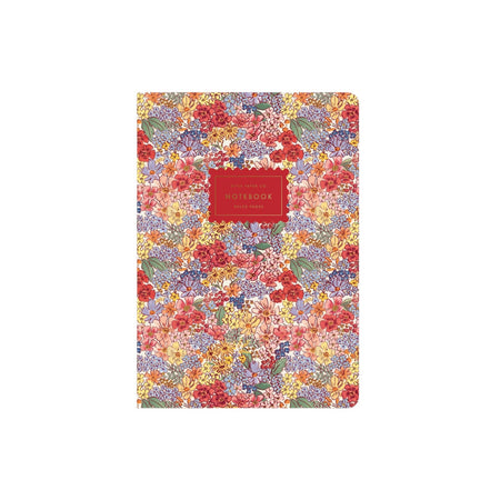 A floral notebook with a dense multicolor pattern of red, yellow, purple, and green flowers on a light background, featuring a red rectangular label in the center with gold text.
