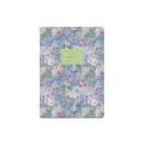 A floral notebook with a dense pattern of purple, blue, and white flowers with green leaves, featuring a light green label on the front that reads ' NOTEBOOK'.