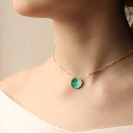 Necklace with a green clover leaf pendant worn by a person on a neutral background
