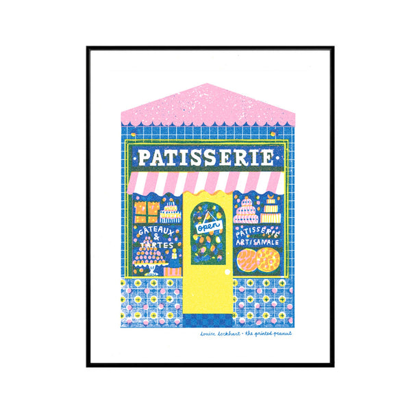 A framed art print featuring a colorful illustration of a French patisserie shop with a pink and white striped awning, blue patterned facade, yellow door, and various illustrated pastries. The print is presented on a white background inside a thin black frame.