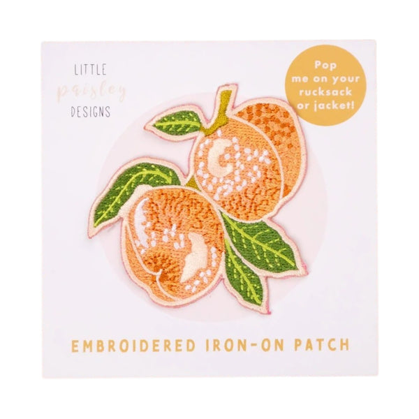 An embroidered iron-on patch of peaches with green leaves, presented on its white backing card. The backing card features the brand name 'Little Paisley Designs' and a yellow circular sticker that reads 'Pop me on your rucksack or jacket!'.