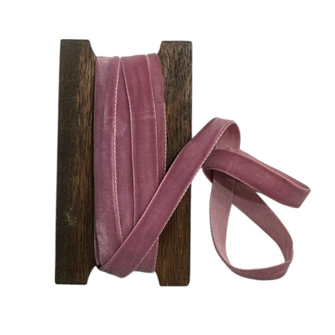 Pink velvet ribbon on a wooden spool against a white background