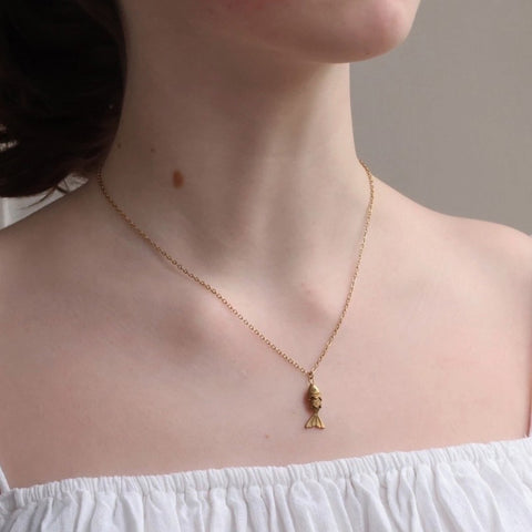 Gold moving fish necklace with a pendant worn by a person against a neutral background