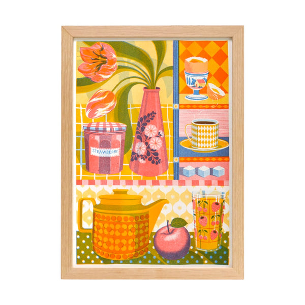 A framed print showing a brightly coloured teapot, vase of tulips, cup and saucer and a eggcup