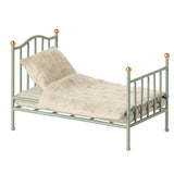 Small green metal bed with bedding on a white background