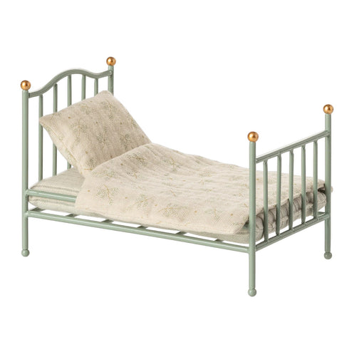 Small green metal bed with bedding on a white background