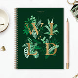 Hard backed 18 month planner with the text WILD printed in gold surrounded by tropical plants and leaves on a dark green background.